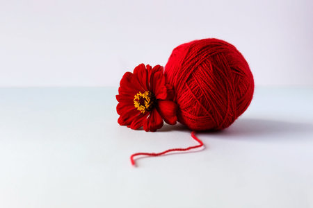 A red ball of thread and a tsinia flower on a green background for knitting red cozy warm things