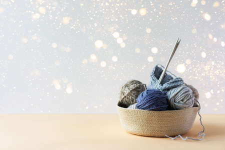 Gray and blue balls of thread in a beige basket with knitting needles for knitting warm clothes with festive lights, knitting hobbyの写真素材
