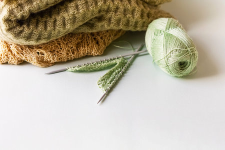 Green yarn thread with knitting needles and finished yarn products on a green background for...