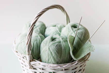 Light green yarn threads in a white basket on a gray background with knitting needles.の写真素材
