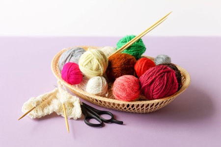 Red, yellow, white, purple, brown, green balls of thread in a beige basket with knitting needles...