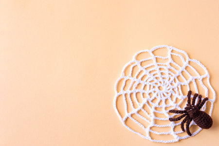 Halloween concept. Knitted black spider and white web on an orange background with space for text,...