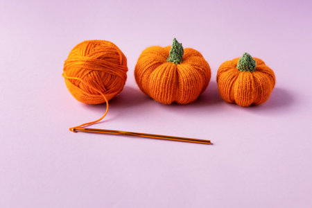 Knitted orange pumpkins and an orange ball of thread with a crochet hook on a purple background, autumn composition, front view. Halloween concept.の写真素材