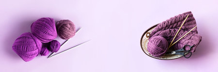 A purple ball of thread and a knitted hat with knitting needles and scissors in a basket on a purple...