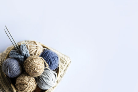Gray, brown and blue balls of knitting threads in a beige basket with knitting needles and a stack...