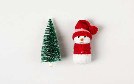 Knitted children toy snowman with a small green Christmas tree on a gray background, the concept of the new year.の写真素材