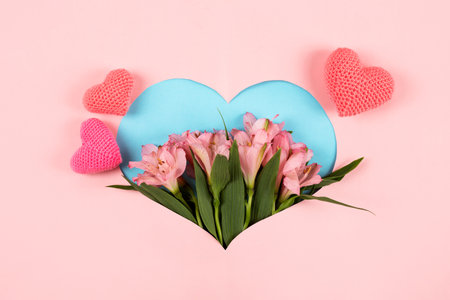 Composition of purple flowers Alstroemeria with a knitted pink heart on a pink background in the shape of a heart. Valentines Day concept, greetings for a loved one, top viewの写真素材