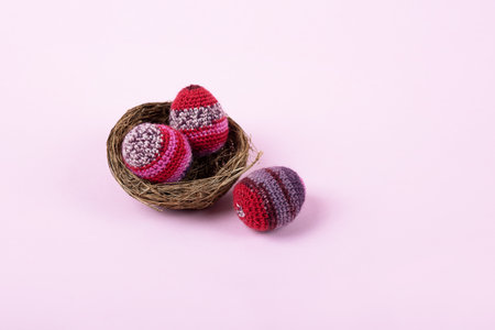 Three knitted Easter decorative eggs in lilac and purple shades in a nest on a purple background. Happy Easter concept. Greeting card with a copy of the place for the text.の写真素材