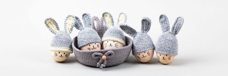 Five Easter eggs with funny faces and gray crocheted hats with bunny ears in a decorative basket on...