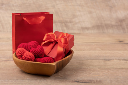 Red knitted hearts and gift box in a wooden bowl in the shape of a heart and gift package on a wooden background. Happy Valentines Day, Mothers Day and birthday greeting card.の写真素材