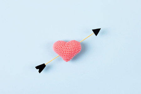 Composition for Valentines day, greeting card. Knitted pink heart and cupids arrow on a blue...