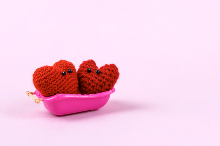 Two knitted hearts with cute faces are washing in a pink bathroom. Love concept. Staged life story of a heart in its roomの写真素材
