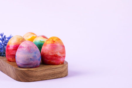 Colorful Easter eggs in a wooden egg stand on a lilac background. Happy Easter concept. Greeting...