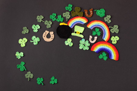 St Patricks Day concept. Knitted composition of a green hat, a pot of gold, a horseshoe, a rainbow and green shamrocks on a black backgroundの写真素材