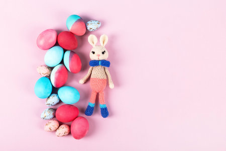 Painted Easter eggs in crimson and blue with crocheted easter bunny on a pink background with a...