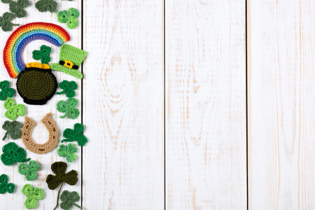St Patricks Day concept. Knitted composition of a green hat, a pot of gold, a horseshoe, a rainbow and green shamrocks on a white wooden background. Copy space, flat layの写真素材