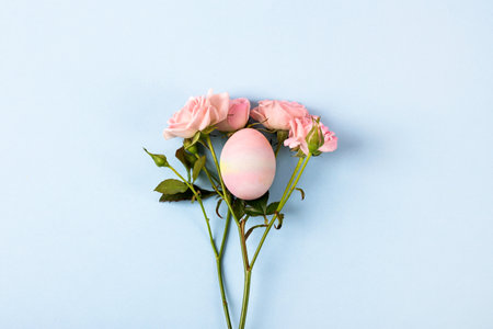 Pale pink Easter egg with a sprig of pink roses on a blue background. Happy Easter concept. Greeting card, copy spaceの写真素材