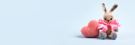 Knitted gray bunny with a crocheted pink heart on a blue background. Banner