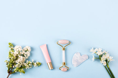 Pink jade roller and gua sha for face massage with cream or gel for the face and flowers daffodils and lilacs. Facial massager tools. Anti age, lifting and toning care. Modern selfcare concept.の写真素材