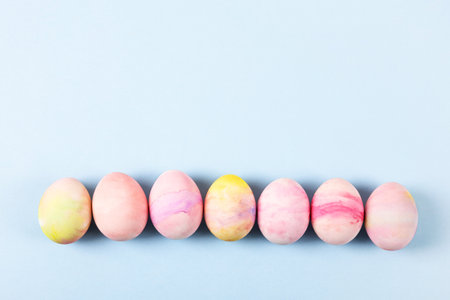 Painted Easter eggs in pink yellow and green on a blue background with a place for text. Happy Easter concept. Greeting card.の写真素材