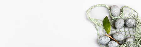 Grey Easter eggs with a sprig and a magnolia leaf in a green string bag on a grey background. Minimalism, copy space, flat lay, bannerの写真素材