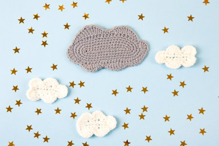 Knitted toys clouds and yellow stars on blue background. Baby stuff and accessories. Top view, flat...