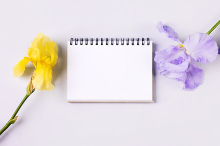 Notebook with clean page with purple and yellow flowers irises on orange background. Flat lay style.の写真素材