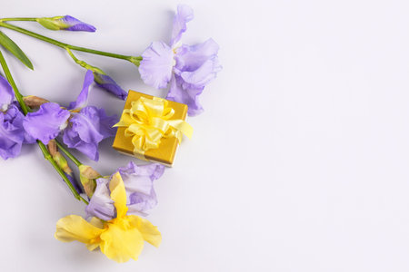 Greeting card for mothers day, Valentines Day, birthday. Yellow gift box with a satin ribbon bow and purple iris flowers on a blue background with a place for your text.の写真素材