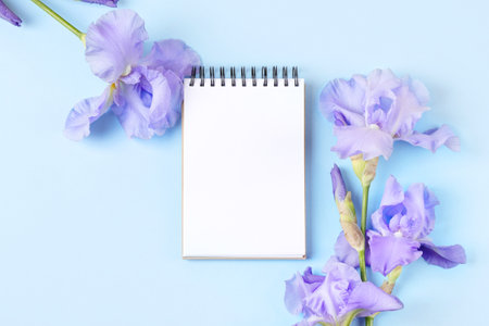 Notebook with clean page with purple flowers irises on orange background. Flat lay style.の写真素材