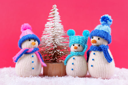 Three knitted snowmen on a magenta background in blue and pink hats. Merry Christmas and New Year 2024 greeting cardの写真素材