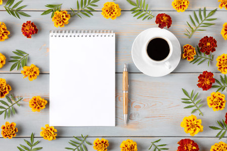 Composition with opened blank notepad and pen, cup of black coffee, orange flowers and leaves...