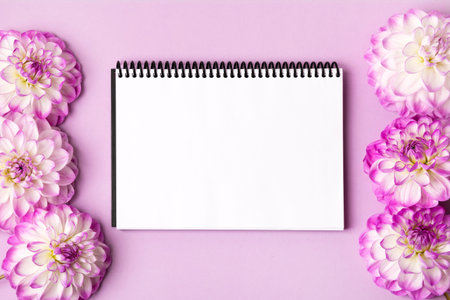 Notebook with clean page with purple flowers dahlias on lilac background. Colorful autumn flower background with space for text. Nature trendy decorative design. Flat lay.の写真素材