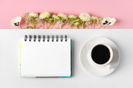 Composition with opened blank notepad, cup of black coffee, aster flowers and pansies on a gray and...