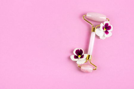Pink jade roller for face massage with flowers pansies. Facial massager tools. Anti age, lifting and toning care. Modern selfcare concept.の写真素材