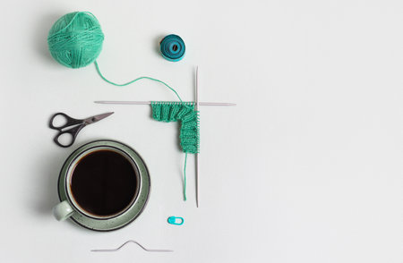 Composition of homemade needlework from cup of black coffee, scissors, mint ball for knitting and knitting needles, centimeter, pin. Hobbies of knitting warm clothes, toys, things for house.の写真素材