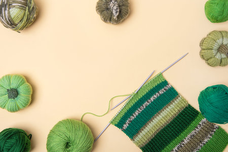 Green knitting balls with knitting needles on beige background. Set for the hobby of knitting warm...