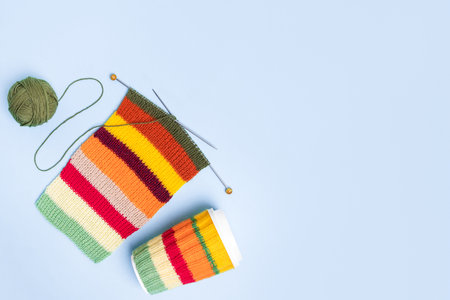 Cup for takeaway coffee with knitted autumn striped cover and knitted wool with knitting needles on blue background. Concept of takeaway coffee, walking, energetic life, hobbies needleworkの写真素材