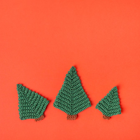 Christmas festive green knitted trees on red background. Winter knitting creativity. Holiday...