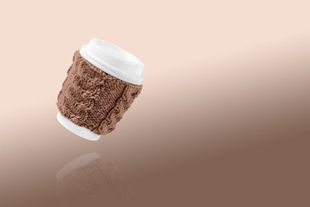 Cup made of cardboard for takeaway coffee with knitted cover and white lid. Concept of takeaway coffee, walking, energetic life. Demonstrating the colors of 2025 - Mocha Mousse.の写真素材