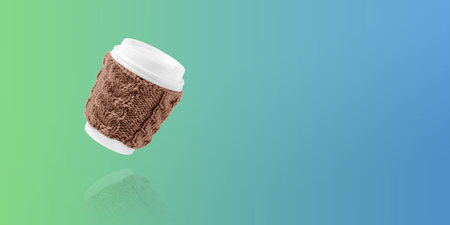 Cup for takeaway coffee with knitted brown cover on blue and green gradient background. Concept of takeaway coffee, walking, energetic lifeの写真素材