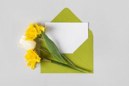 Green envelope with clean white sheet of paper for your text and spring flowers on gray background. Invitation to the holidays. Flat lay.の写真素材