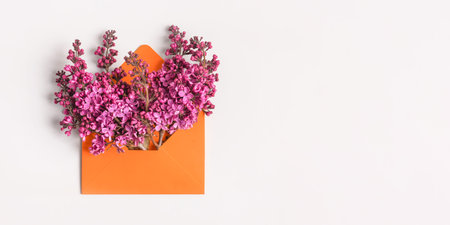 Orange envelope with spring flowers purple lilac on gray background. Invitation to the holidays....