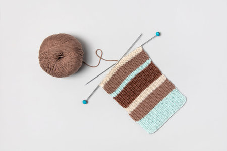 Brown beige and turquoise piece of striped knitting with knitting needles and ball of brown thread...
