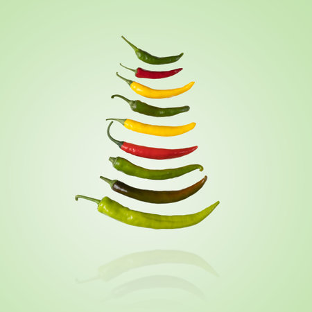 Red, green and yellow hot pepper flying in the air on a green background. Healthy food, fresh healthy vegetables from the gardenの写真素材