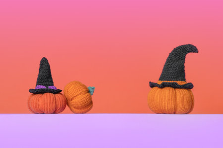 Knitted orange pumpkins with black witch hat on purple podium and orange purple gradient background, autumn composition, front view. Halloween concept.の写真素材