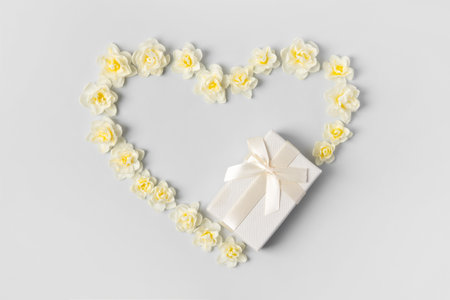 Romantic composition in shape of heart of white daffodils and gift box with satin bow on gray background. Holiday greeting card, an invitation to celebration. Flat lay, copy spaceの写真素材