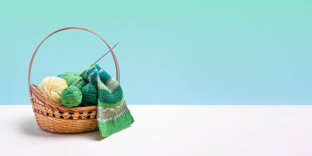 Green knitting balls in a basket with knitting needles on beige table. Set for the hobby of knitting warm clothes or toys. Concept needlework. Bannerの写真素材