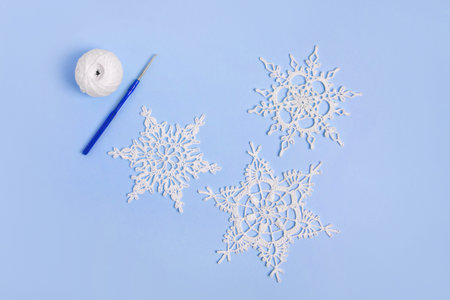 White crocheted snowflake, a ball of thread and a crochet hook on a blue background. Knitting decorative ornaments for Christmas and New Year. Top view, flat lay.の写真素材