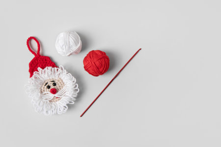 Crocheted toy Santa Claus in a red hat with balls of thread and crochet hook on gray background. Baby stuff and accessories. Gift for winter holidays. Top view, flat lay.の写真素材