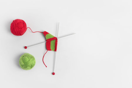 Red knitted wool on gray background with knitting needles for knitting warm clothes and hobbies needlework. Knitting a striped Christmas scarf with red and green threadsの写真素材